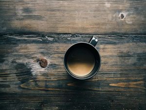 A cup of coffee in a black mug on top of a dark wooden table.