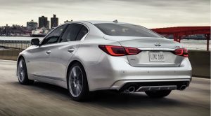 A silver 2020 INFINITI Q50 being driven on a road with a body of water, dock, and building far off in the background. | INFINITI dealer in Ellisville, MO
