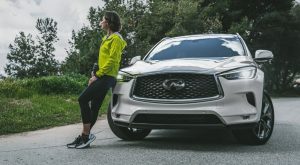 A woman dressed in workout gear leaning against the front passenger side of a white 2020 INFINITI QX50. | INFINITI dealer in Ellisville, MO