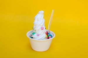 Vanilla frozen yogurt with colorful candy in a cup with a yellow background.