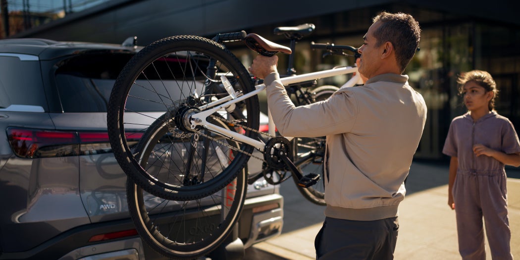 A man is loading a bicycle onto a car bike rack while a young girl watches.